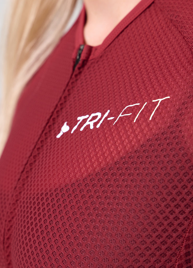 Close-up of TRI-FIT logo printed on the chest of the VANGUARD tri-suit in wine red, showing textured breathable fabric
